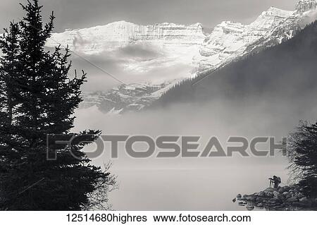 Silhouette of a photographer on the shore of Lake Louise with fog rising from the lake at sunrise, Banff National Park; Lake Louise, Alberta, Canada View Large Photo Image Stock Photograph - Silhouette of a photographer on the shore of Lake Louise with fog rising from the lake at sunrise, Banff National Park; Lake Louise, Alberta, Canada. Fotosearch