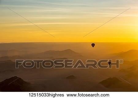 Silhouette of hot air balloons in the golden sky over the sand dunes at sunrise in the Namib Desert; Sossusvlei, Hardap Region, Namibia View Large Photo Image Stock Photograph - Silhouette of hot air balloons in the golden sky over the sand dunes at sunrise in the Namib Desert; Sossusvlei, Hardap Region, Namibia. Fotosearch