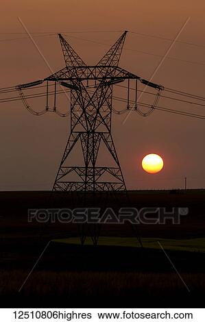 Stock Photograph - Silhouette of large metal electrical tower with power lines and orange sun ball; Blackie, Alberta, Canada. Fotosearch