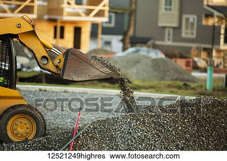 Stock Photograph - Small front end loader moving and placing gravel in a park area for new home construction; Langley, British Columbia, Canada. Fotosearch