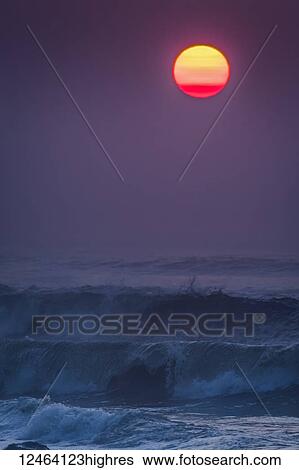 Stock Photograph - Smoke in the air colors the sun on a summer evening; Seaside, Oregon, United States of America. Fotosearch