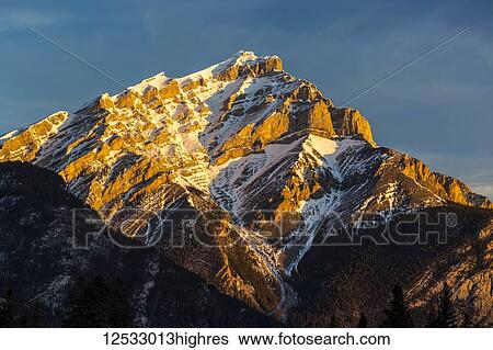 Snow-covered mountain peak glowing with warm sunrise light and blue sky; Banff, Alberta, Canada View Large Photo Image Stock Photograph - Snow-covered mountain peak glowing with warm sunrise light and blue sky; Banff, Alberta, Canada. Fotosearch