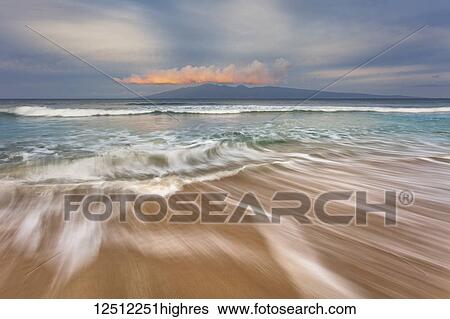 Stock Photograph - Soft water stretches across the sand at sunrise with a view of Molokai; Maui, Hawaii, United States of America. Fotosearch