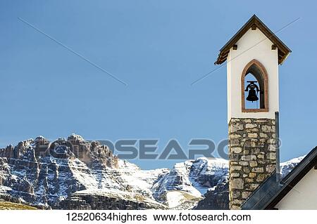 Stock Photograph - Stone church bell tower with snow-covered mountain range in the background with blue sky; Sesto, Bolzano, Italy. Fotosearch