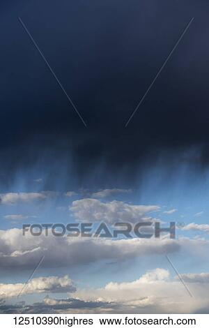 Stock Photograph - Storm clouds dropping rain in the foreground with blue sky and cloud in the distance; Idaho, United States of America. Fotosearch