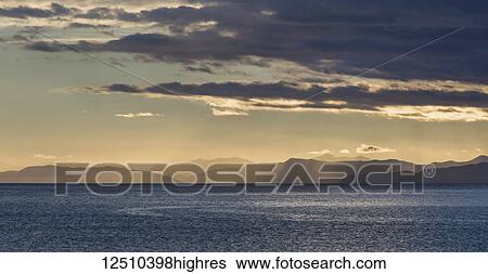 Sun rays shining through clouds over the mountains and ocean at sunrise, Abel Tasman National Park; New Zealand View Large Photo Image Stock Photograph - Sun rays shining through clouds over the mountains and ocean at sunrise, Abel Tasman National Park; New Zealand. Fotosearch