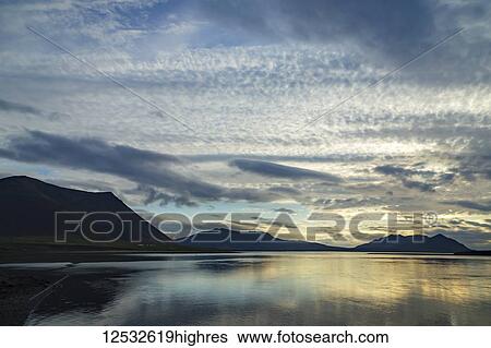 Stock Photograph - Sunset and cloudy skies over a remote ocean inlet in Western Iceland on the Snaefellsnes Peninsula; Iceland. Fotosearch