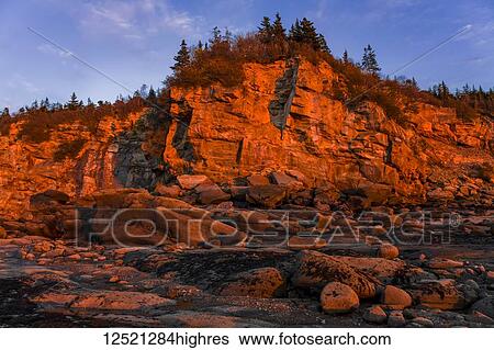 Stock Photograph - Sunset illuminates the rugged coastline adjacent to Sand River Beach; Nova Scotia, Canada. Fotosearch