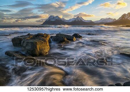 Stock Photograph - Sunset over the mountains of the Strandir Coast, Iceland as the surf pounds the shoreline; West Fjords, Iceland. Fotosearch