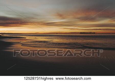 Stock Photograph - Sunset washes gold and orange over the ocean and beach; Long Beach, California, United States of America. Fotosearch