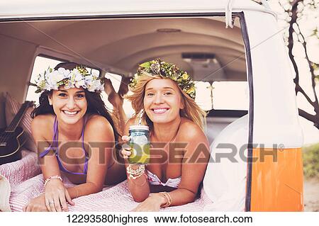 Stock Photograph - Surfer Girls Beach Lifestyle; Beautiful Surfer Girls Relaxing In The Back Of Classic Vintage Surf Van On The Beach At Sunset. Fotosearch