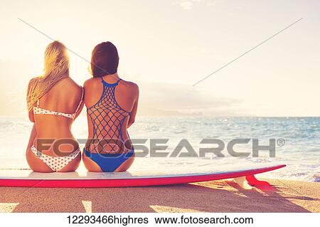 Stock Photograph - Surfer Girls On The Beach At Sunset. Summer Outdoor Lifestyle. Best Friends Hanging Out On The Beach.. Fotosearch