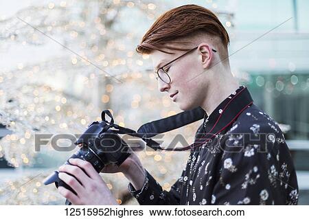 Stock Photograph - Teenage boy looking at the digital photographs on the screen of his camera; Vancouver, British Columbia, Canada. Fotosearch