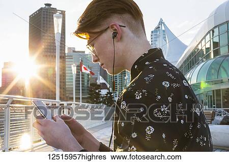 Teenage boy using his smart phone and wearing earbuds in downtown Vancouver; Vancouver, British Columbia, Canada View Large Photo Image Stock Photograph - Teenage boy using his smart phone and wearing earbuds in downtown Vancouver; Vancouver, British Columbia, Canada. Fotosearch