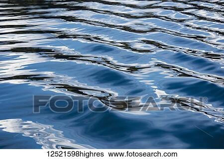 Stock Photograph - The blue, black, and white reflections of the sky, clouds, and nearby land on the wake of a boat in the Puget Sound, Washington, creating a lovely texture and sense of movement; Puget Sound, Washington, United States of America. Fotosearch