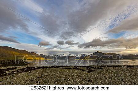 Stock Photograph - The rich colours of the hills are vibrant in the sunset with the ocean reflection in Western Iceland. Fotosearch