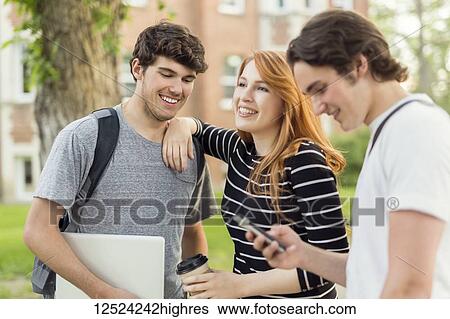 Three friends standing and talking on the university campus with their smart phone and laptop; Edmonton, Alberta, Canada View Large Photo Image Stock Photograph - Three friends standing and talking on the university campus with their smart phone and laptop; Edmonton, Alberta, Canada. Fotosearch