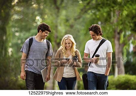 Stock Photograph - Three friends walking and talking on the university campus; Edmonton, Alberta, Canada. Fotosearch