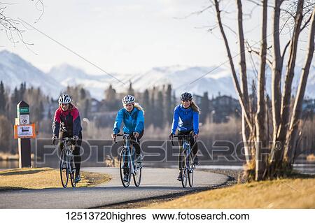 Stock Photograph - Three young women riding their bicycles on a trail along the water's edge; Anchorage, Alaska, United States of America. Fotosearch