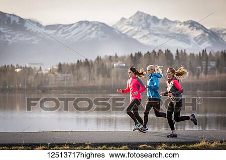 Three young women running on a trail along the water's edge with mountains in the distance; Anchorage, Alaska, United States of America View Large Photo Image Stock Photograph - Three young women running on a trail along the water's edge with mountains in the distance; Anchorage, Alaska, United States of America. Fotosearch