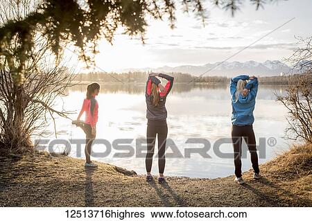 Stock Photograph - Three young women stretching on a trail at the water's edge; Anchorage, Alaska, United States of America. Fotosearch