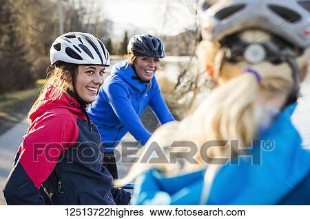 Stock Photograph - Three young women talking while on their bicycles on a trail at sunrise; Anchorage, Alaska, United States of America. Fotosearch