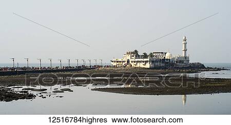 Stock Photograph - Tourists on a road leading to a building and tower along the coast, Arabian Sea; Mumbai, Maharashtra, India. Fotosearch