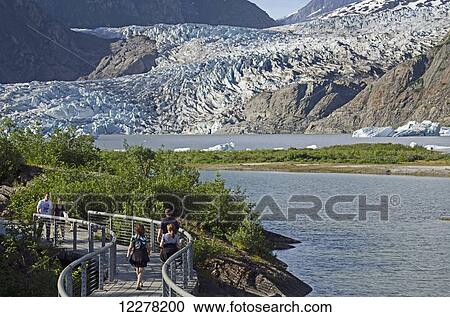 Stock Image - Tourists walk along paved path viewing Mendenhall Glacier in Tongass National Forest, Southeast Alaska, summer. Fotosearch