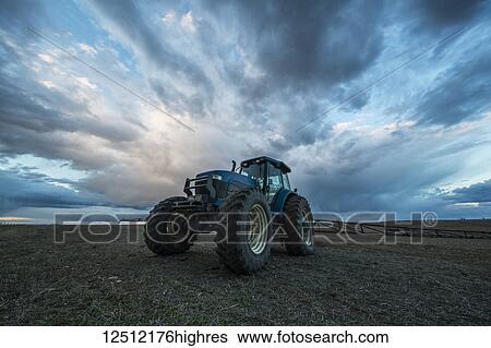 Stock Photograph - Tractor parked in a field under a dramatic sky at sunset; Val Marie, Saskatchewan, Canada. Fotosearch