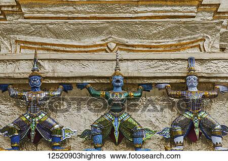Stock Photograph - Traditional Thai figures along a stone wall at a Buddhist temple; Thailand. Fotosearch