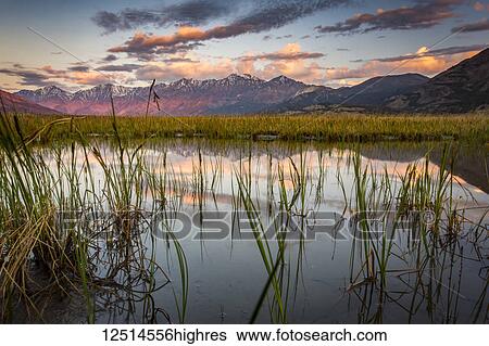 Stock Photograph - Tranquil landscape at sunrise of reflections in water in the foreground and a mountain range in the distance, Kluane National Park and Reserve; Destruction Bay, Yukon, Canada. Fotosearch