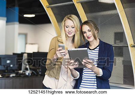 Two beautiful young millennial business women using technology in the workplace; Sherwood Park, Alberta, Canada View Large Photo Image Stock Photograph - Two beautiful young millennial business women using technology in the workplace; Sherwood Park, Alberta, Canada. Fotosearch