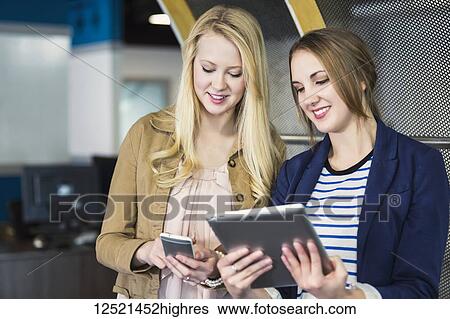 Two beautiful young millennial business women using technology in the workplace; Sherwood Park, Alberta, Canada View Large Photo Image Stock Photograph - Two beautiful young millennial business women using technology in the workplace; Sherwood Park, Alberta, Canada. Fotosearch