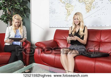 Two beautiful young millennial business women sitting in a workplace on red leather furniture using their handheld devices while waiting for a job interview; Sherwood Park, Alberta, Canada View Large Photo Image Stock Photograph - Two beautiful young millennial business women sitting in a workplace on red leather furniture using their handheld devices while waiting for a job interview; Sherwood Park, Alberta, Canada. Fotosearch