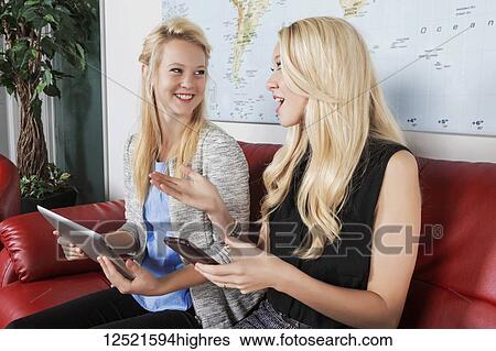 Two beautiful young millennial business women sitting in a workplace on red leather furniture using their handheld devices while waiting for a job interview; Sherwood Park, Alberta, Canada View Large Photo Image Stock Photograph - Two beautiful young millennial business women sitting in a workplace on red leather furniture using their handheld devices while waiting for a job interview; Sherwood Park, Alberta, Canada. Fotosearch