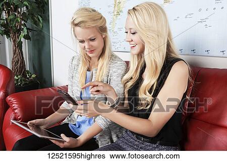 Two beautiful young millennial business women sitting in a workplace on red leather furniture using their handheld devices while waiting for a job interview; Sherwood Park, Alberta, Canada View Large Photo Image Stock Photograph - Two beautiful young millennial business women sitting in a workplace on red leather furniture using their handheld devices while waiting for a job interview; Sherwood Park, Alberta, Canada. Fotosearch