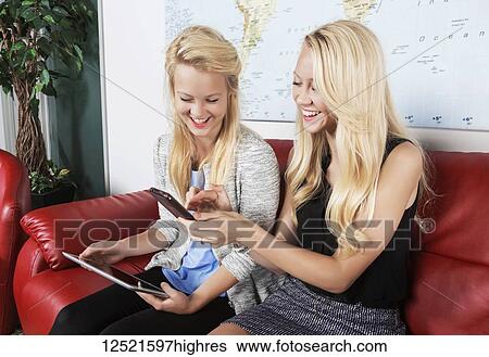 Two beautiful young millennial business women sitting in a workplace on red leather furniture using their handheld devices while waiting for a job interview; Sherwood Park, Alberta, Canada View Large Photo Image Stock Photograph - Two beautiful young millennial business women sitting in a workplace on red leather furniture using their handheld devices while waiting for a job interview; Sherwood Park, Alberta, Canada. Fotosearch