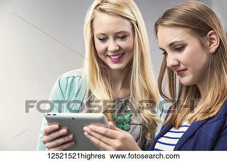 Stock Photograph - Two beautiful young women that are millennial business professionals working together and looking at a tablet at their workplace; Sherwood Park, Alberta, Canada. Fotosearch