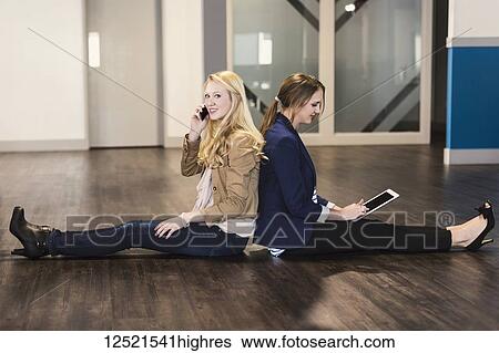 Two beautiful young women who are millennial business professionals sitting back to back on the floor of their workplace using technology; Sherwood Park, Alberta, Canada View Large Photo Image Stock Photograph - Two beautiful young women who are millennial business professionals sitting back to back on the floor of their workplace using technology; Sherwood Park, Alberta, Canada. Fotosearch