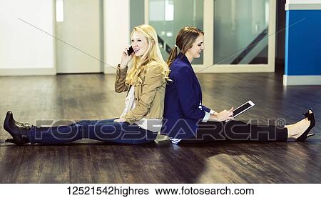 Two beautiful young women who are millennial business professionals sitting back to back on the floor of their workplace using technology; Sherwood Park, Alberta, Canada View Large Photo Image Stock Photograph - Two beautiful young women who are millennial business professionals sitting back to back on the floor of their workplace using technology; Sherwood Park, Alberta, Canada. Fotosearch