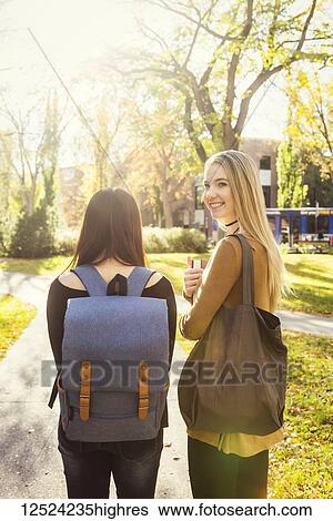 Stock Photograph - Two female student friends walk together on a university campus, one young woman glancing back towards the camera; Edmonton, Alberta, Canada. Fotosearch