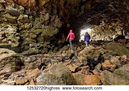 Stock Photograph - Two female tourists hiking through the lava tube caves; Iceland. Fotosearch