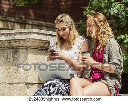 Two female university students sitting together and using their technology outside on the campus; Edmonton, Alberta, Canada View Large Photo Image Stock Photograph - Two female university students sitting together and using their technology outside on the campus; Edmonton, Alberta, Canada. Fotosearch