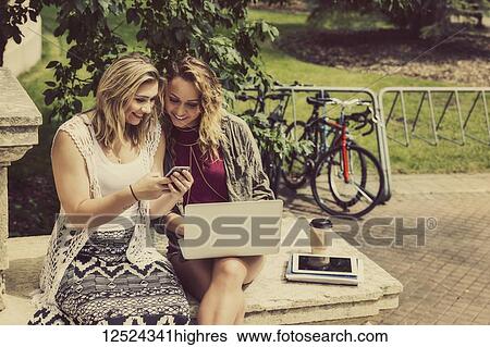 Two female university students sitting together and using their smart phone and laptop computer while sitting on the steps of a campus building; Edmonton, Alberta, Canada View Large Photo Image Stock Photograph - Two female university students sitting together and using their smart phone and laptop computer while sitting on the steps of a campus building; Edmonton, Alberta, Canada. Fotosearch