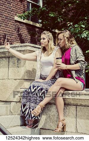 Stock Photograph - Two female university students sitting together on the campus taking a self-portrait with their smart phone and making silly pouty lips; Edmonton, Alberta, Canada. Fotosearch