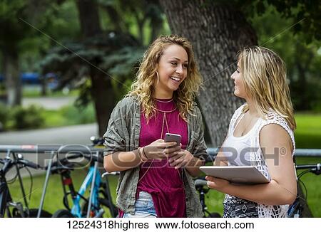 Stock Photograph - Two female university students standing and talking together beside a bike rack on campus; Edmonton, Alberta, Canada. Fotosearch