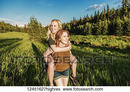 Stock Photograph - Two friends walking in a park, one giving the other a piggy back ride; Edmonton, Alberta, Canada. Fotosearch