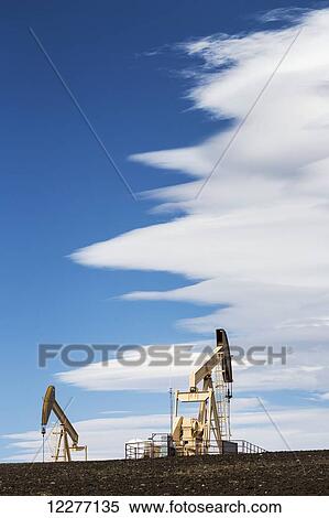 Two pumpjacks on a hill with dramatic clouds in the blue sky; Alberta, Canada View Large Photo Image Stock Photography - Two pumpjacks on a hill with dramatic clouds in the blue sky; Alberta, Canada. Fotosearch