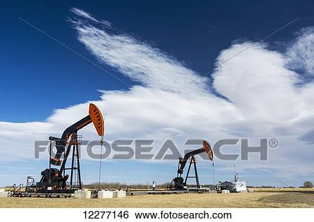 Stock Photograph - Two pumpjacks with dramatic cloud bank and blue sky; Alberta, Canada. Fotosearch