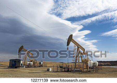 Stock Photo - Two pumpjacks with storm clouds in the distance and some blue sky; Alberta, Canada. Fotosearch
